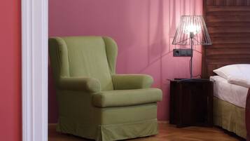 Una habitación con un sillón verde, una mesita de noche con lámpara y una cama con ropa de cama blanca.