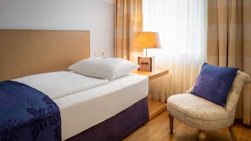 Ein Hotelzimmer mit einem Bett, einem Sessel, einem Nachttisch mit Lampe und einem Vorhangfenster.
