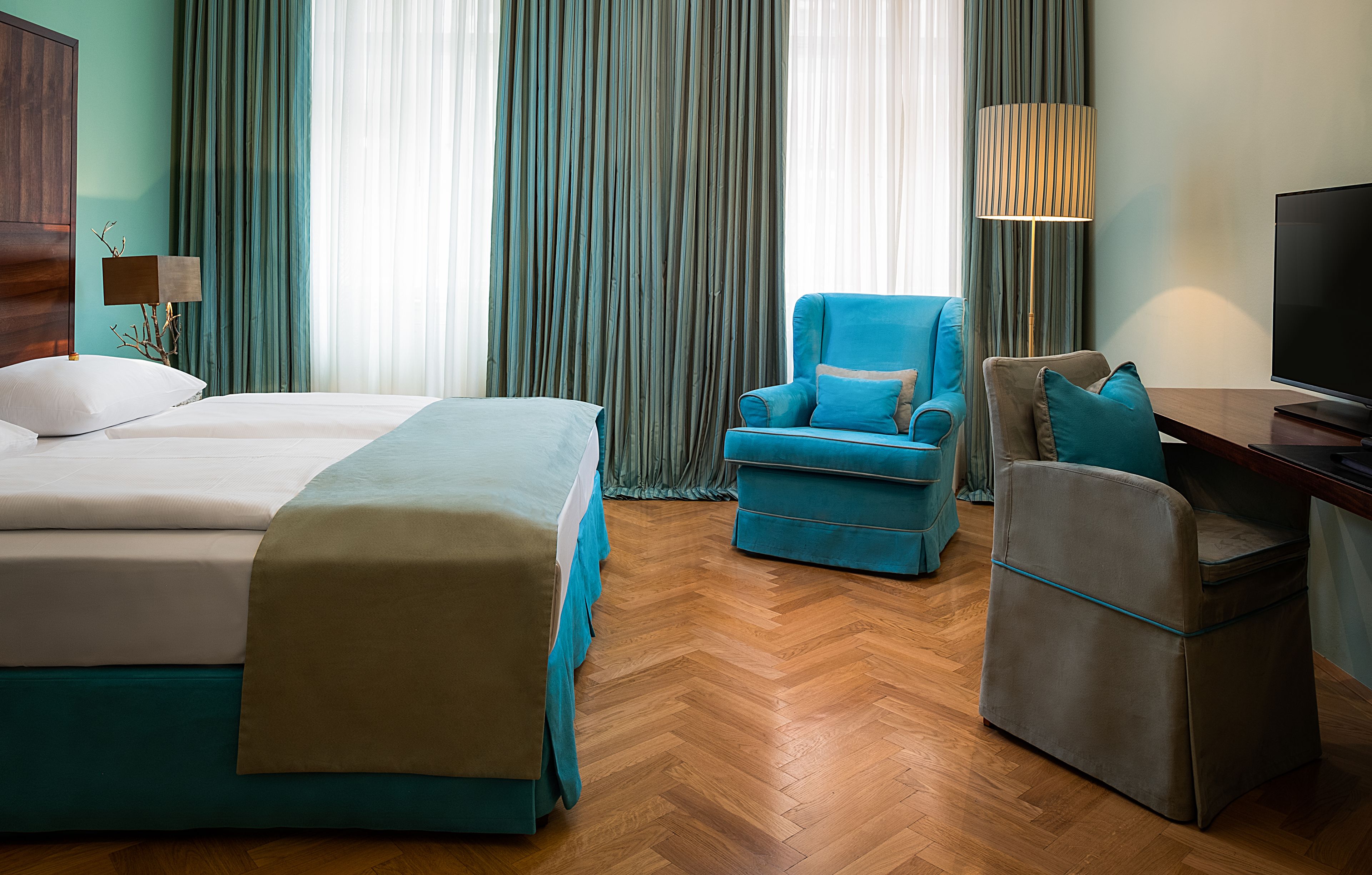 A hotel room with a bed, two armchairs, a desk, and a TV.