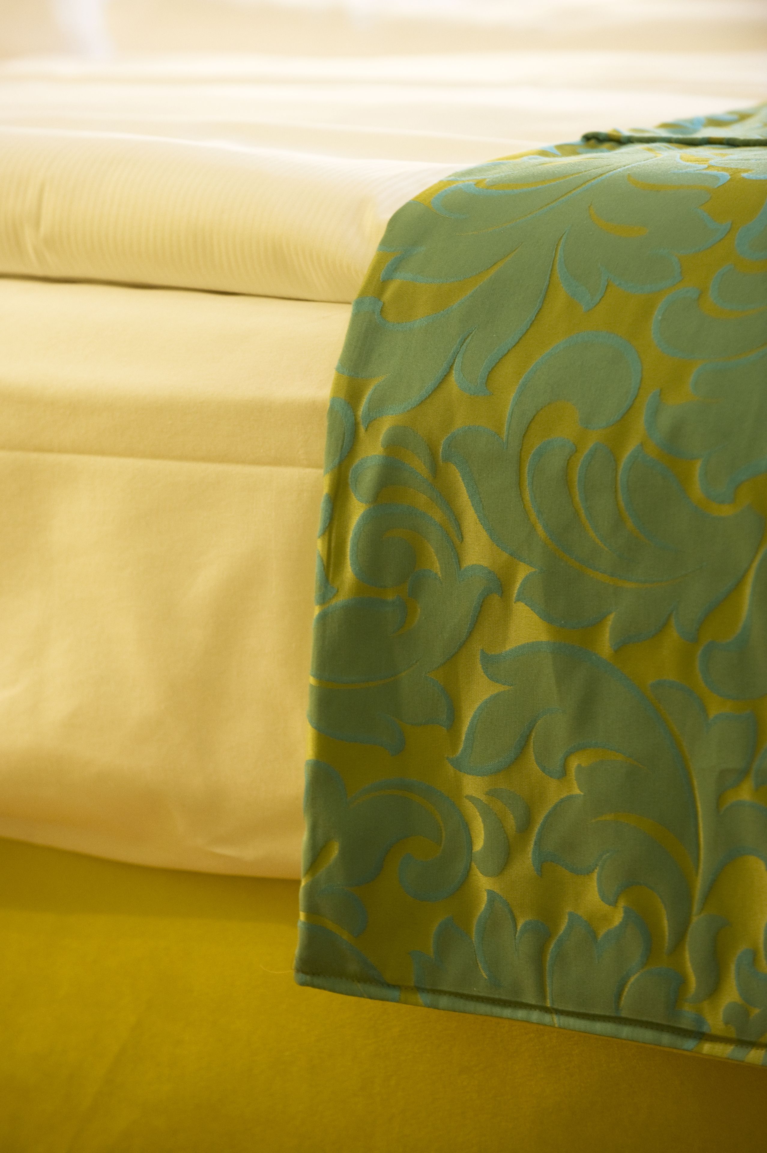 Una cama con una colcha amarilla y un cojín decorativo verde.