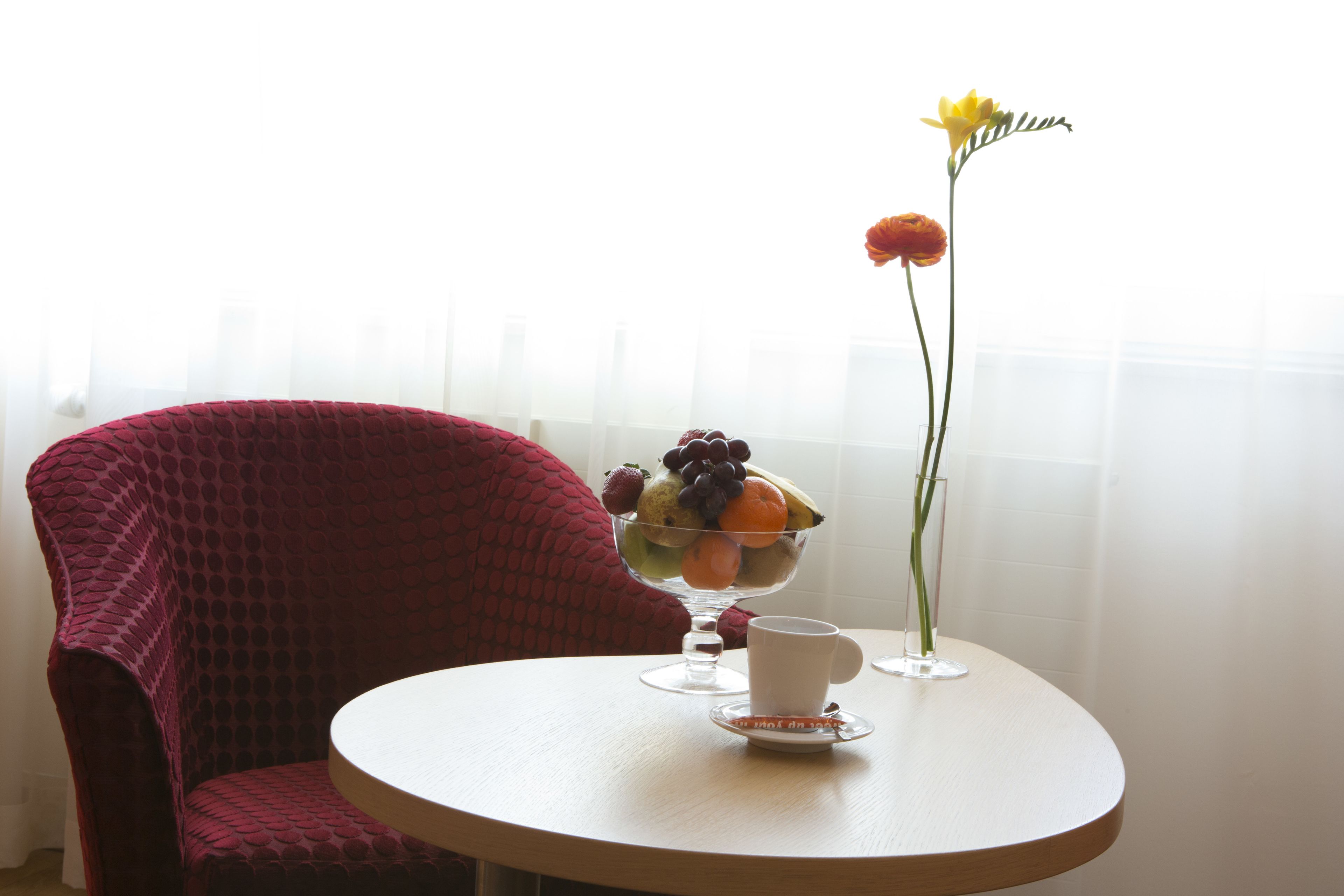 A round table with a fruit bowl, a cup, and a vase with a single flower.