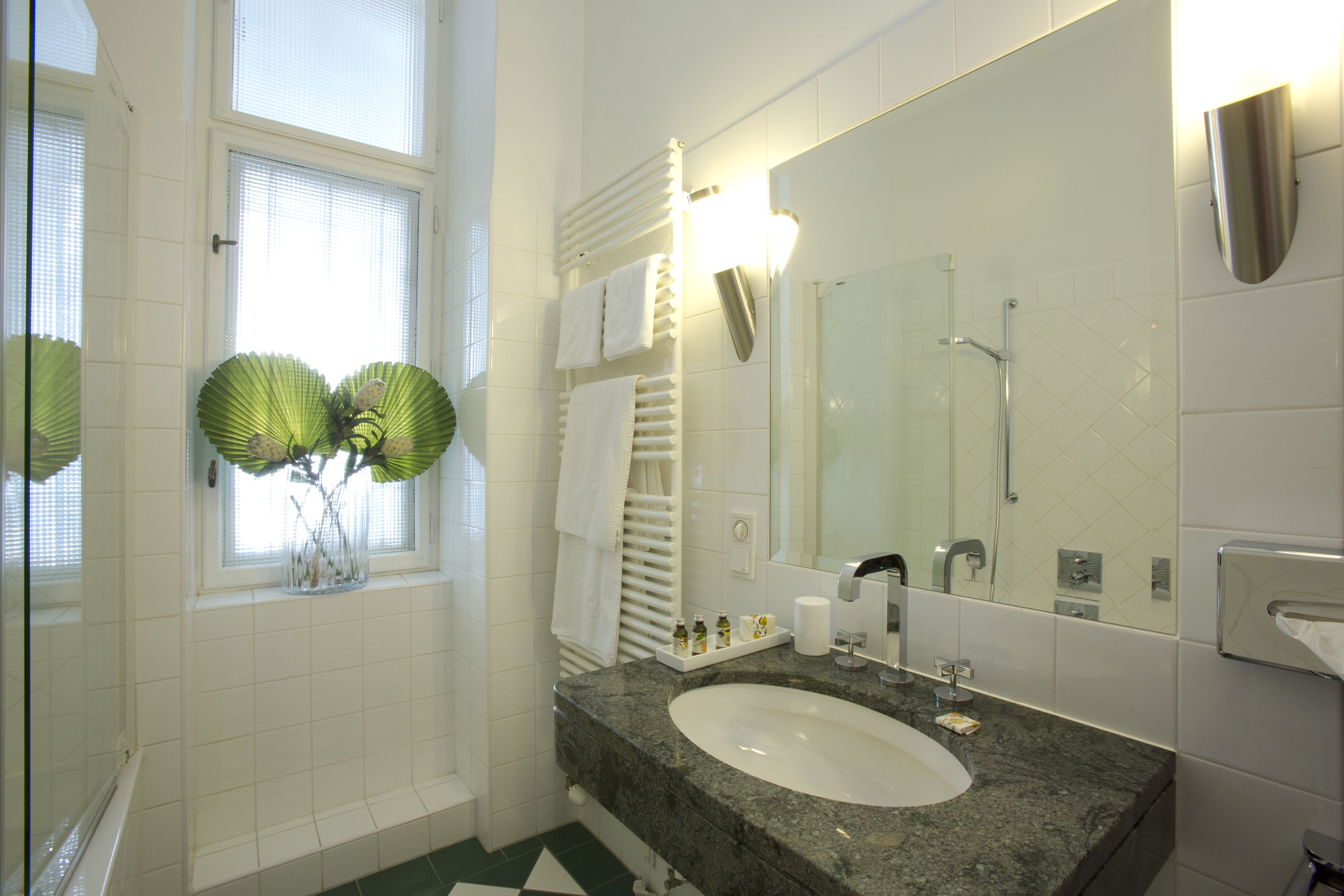 A bathroom with a large mirror, a sink, and a window with blinds.