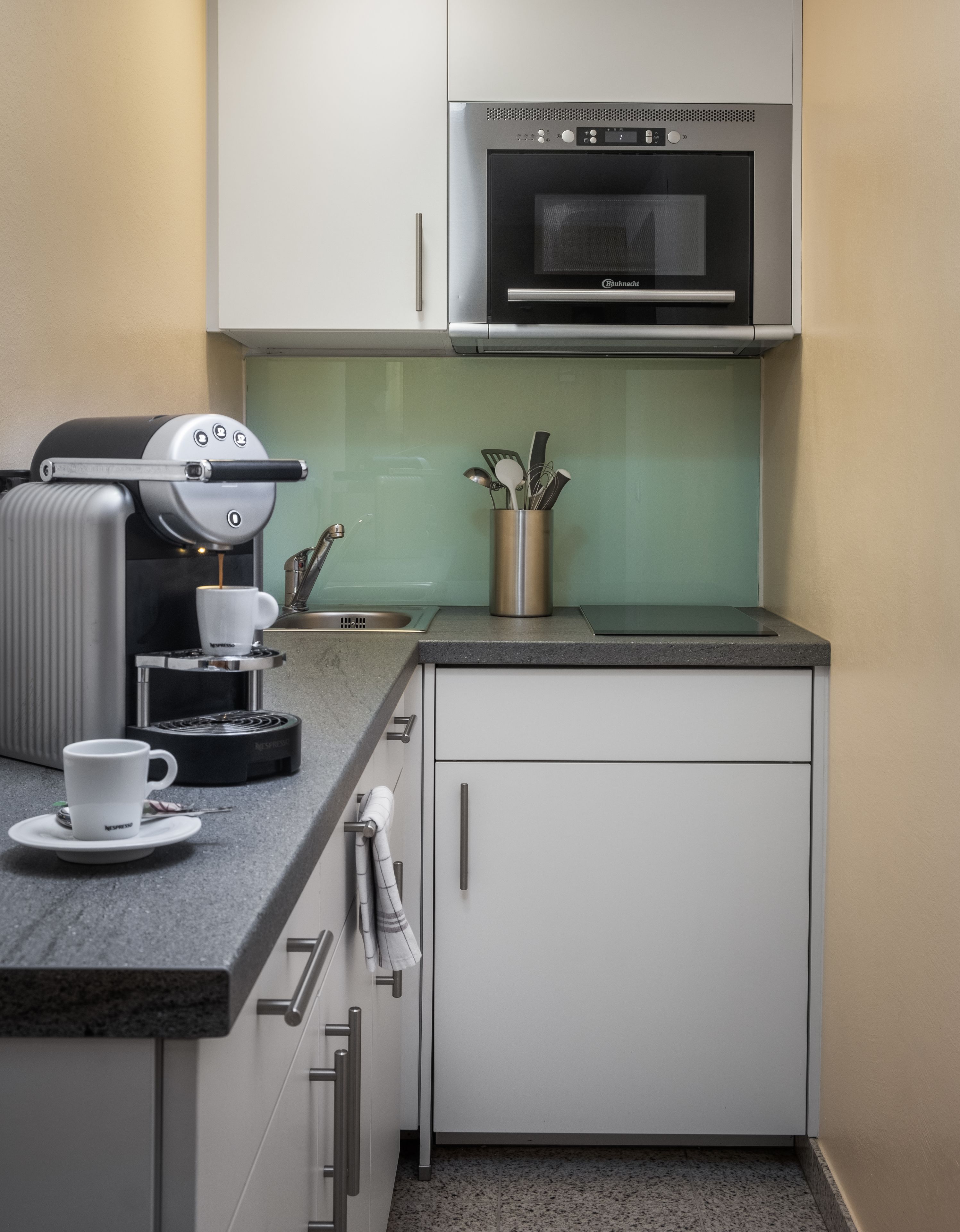 Un angolo cottura compatto con macchina del caffè, forno a microonde e portauoviglie sul piano di lavoro.