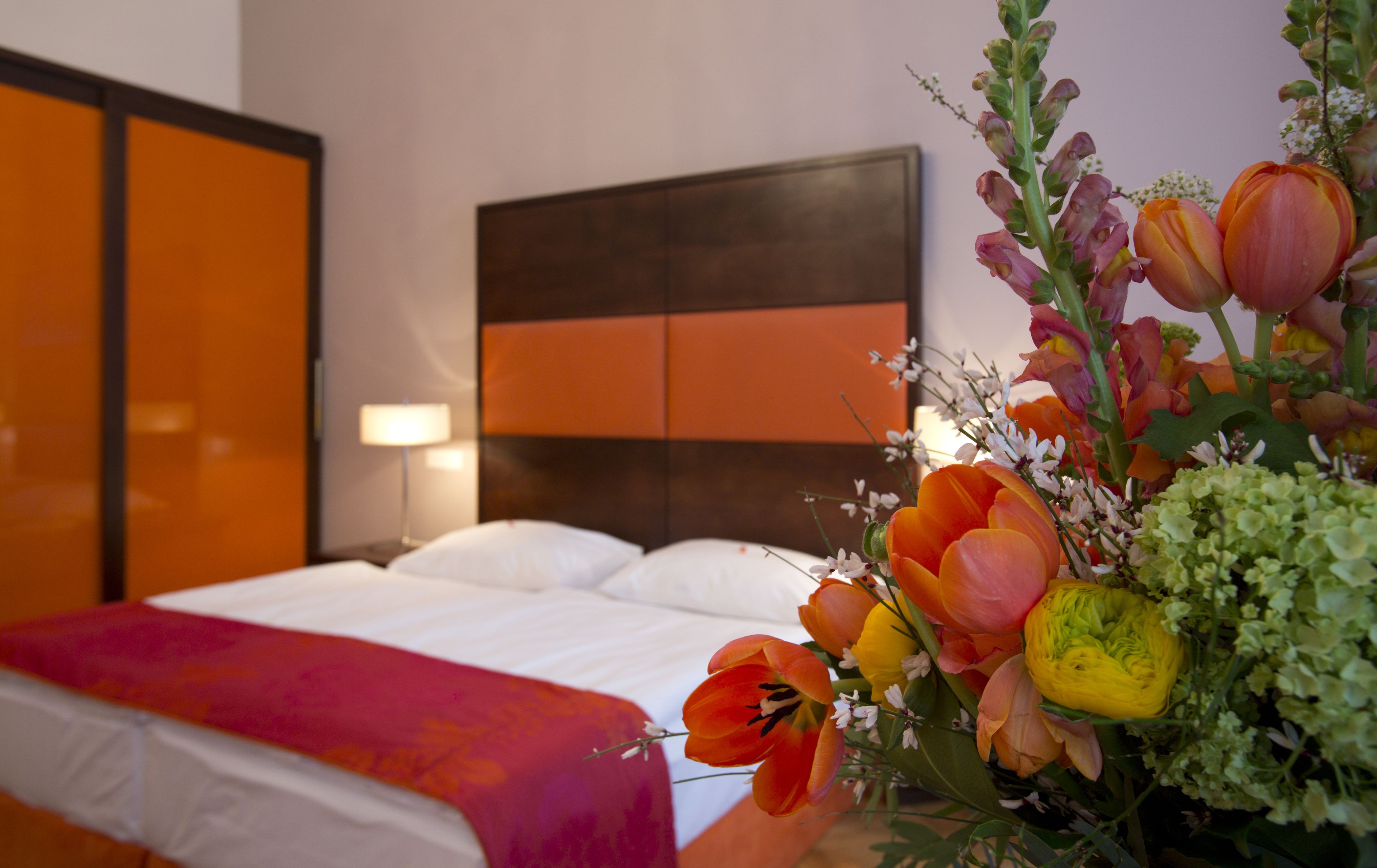 Quarto de hotel com cama, mesa de cabeceira e luminária fixada na parede.