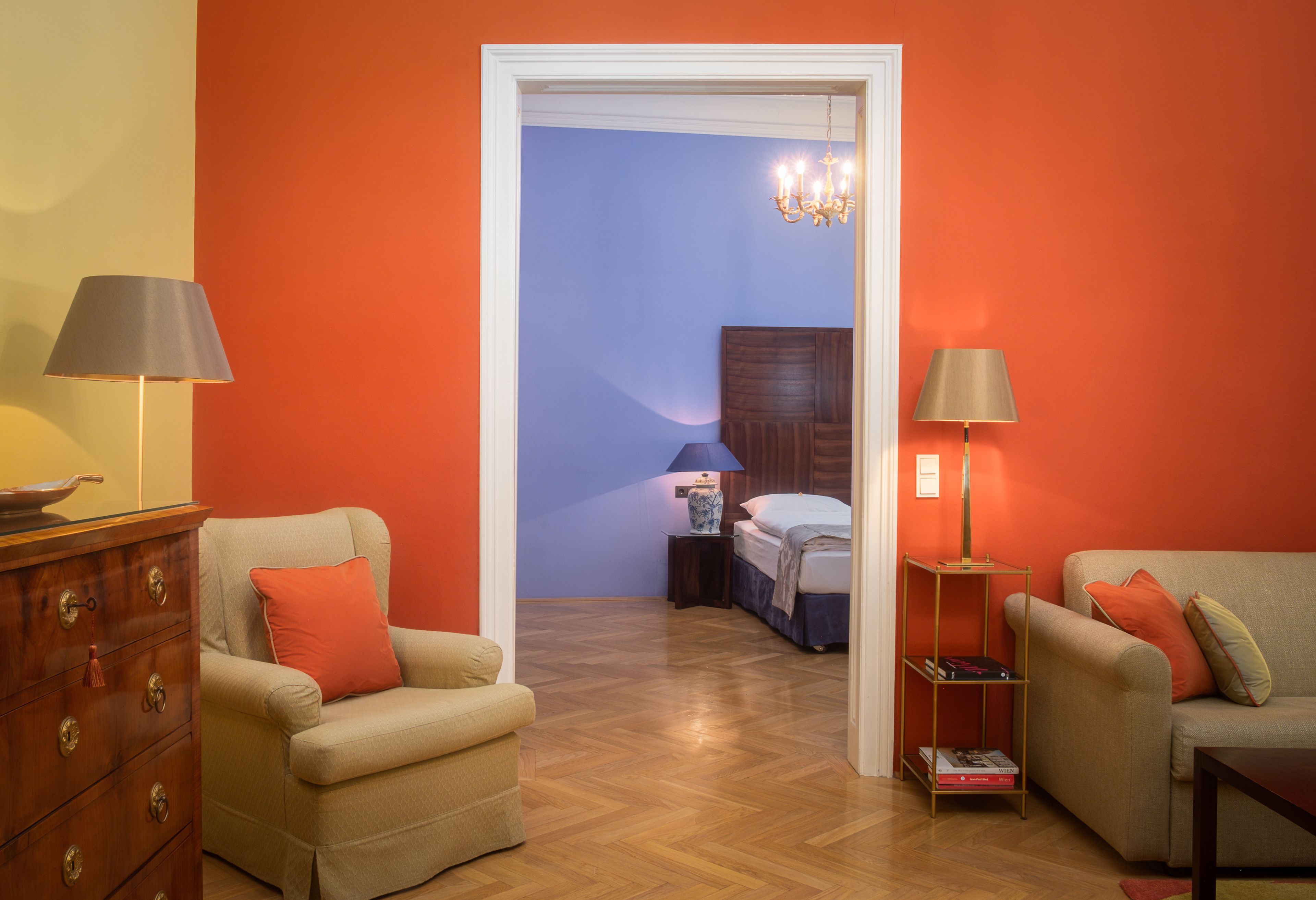Una habitación con cómoda de madera, dos sillones, una estantería y una cama con mesita de noche.