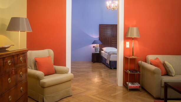 Una habitación con cómoda de madera, dos sillones, una estantería y una cama con mesita de noche.