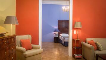 Una habitación con cómoda de madera, dos sillones, una estantería y una cama con mesita de noche.