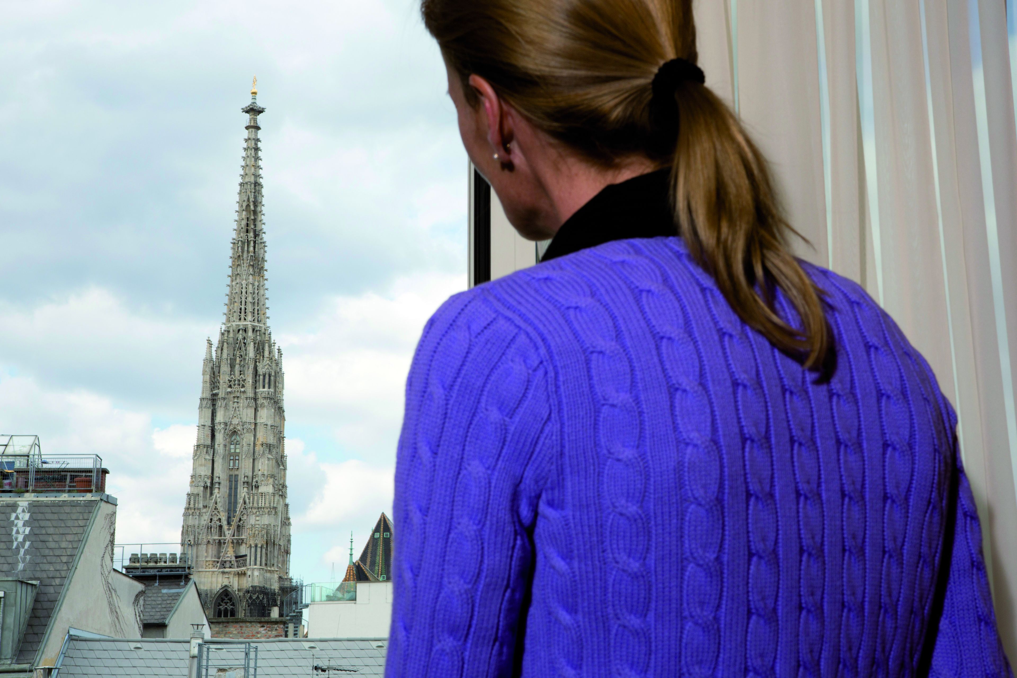 A person in a purple sweater looking out at a tall, Gothic-style church with intricate architecture.