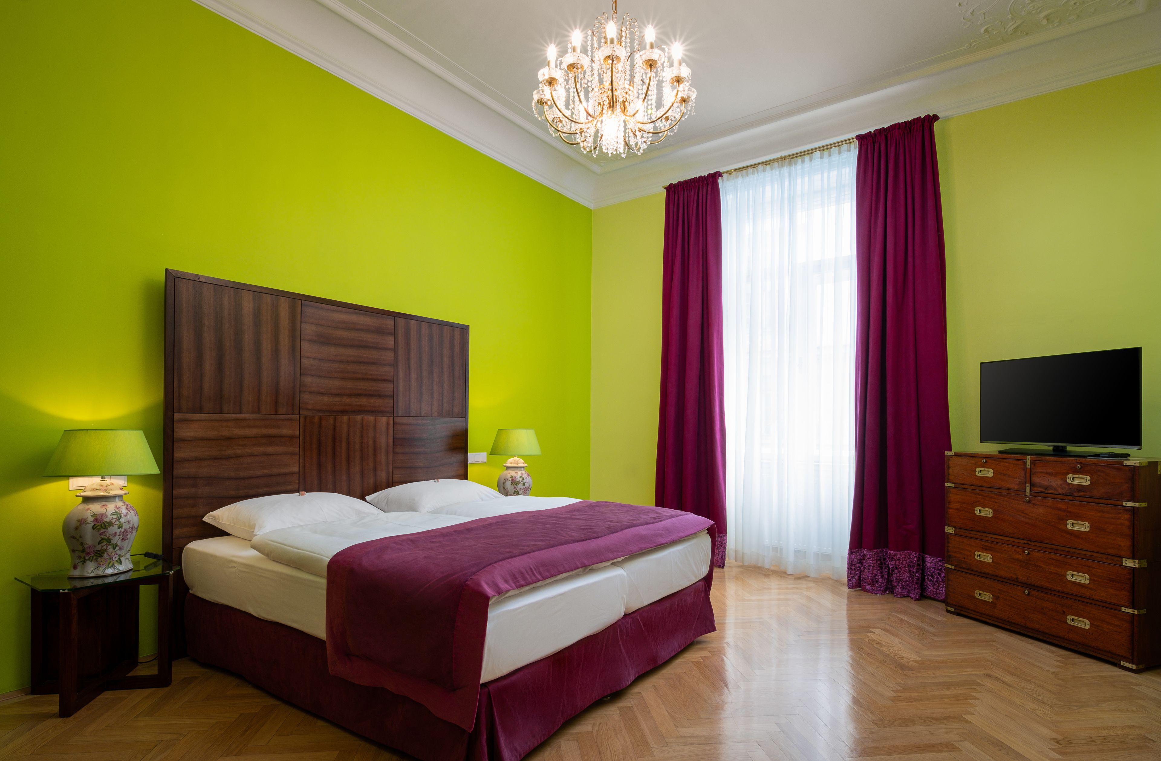 A bedroom with a large bed, two bedside lamps, a wooden dresser, and a television.