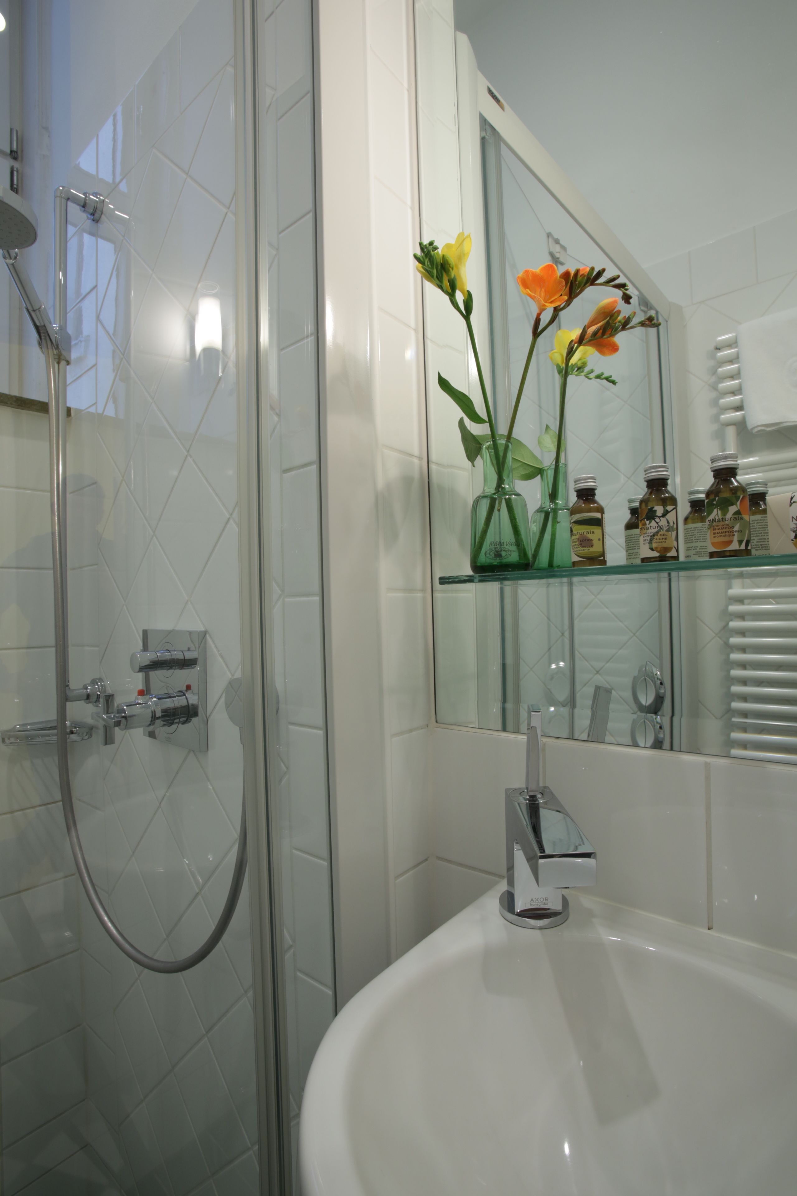 Un baño moderno con cabina de ducha de vidrio, un lavamanos blanco y una repisa de vidrio con artículos de tocador.