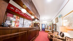 A reception area with a wooden reception desk, a red sign with white text, and a carpeted floor leading to a seating area with upholstered chairs and a table. - Hotel Pension Dormium (Vienna)