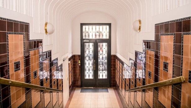 A hallway with a black door, tiled walls, and a staircase with metal railings. - Hotel Pension Dormium (Vienna)