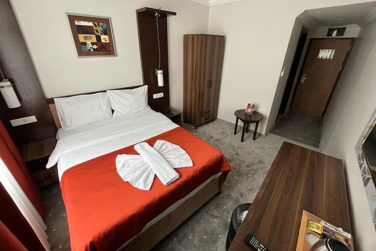 A hotel room with a bed, a desk, a wardrobe, and a small table with a remote control and a tray with items.