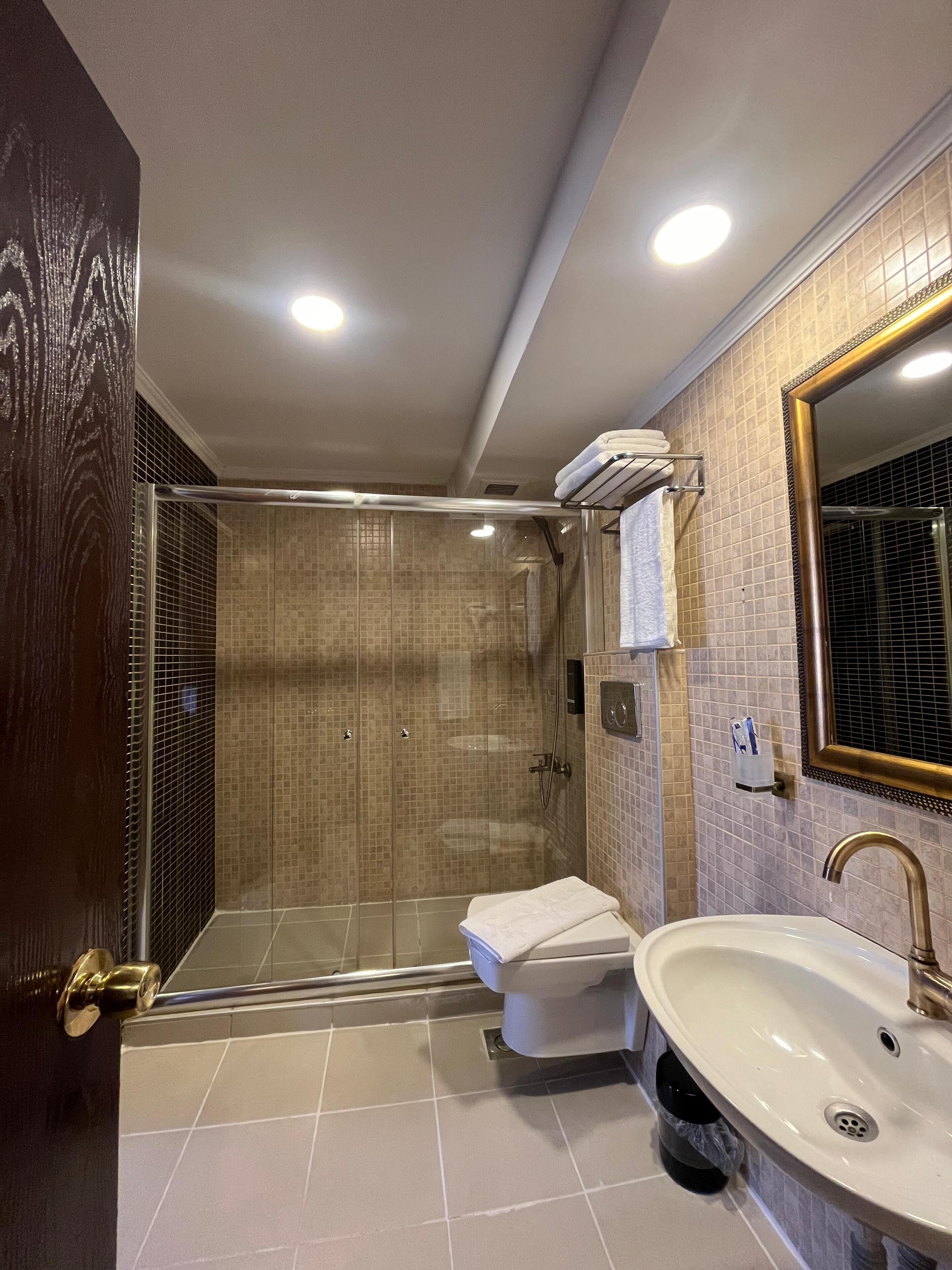 A modern bathroom with a glass-enclosed shower, a white sink, and a large mirror.