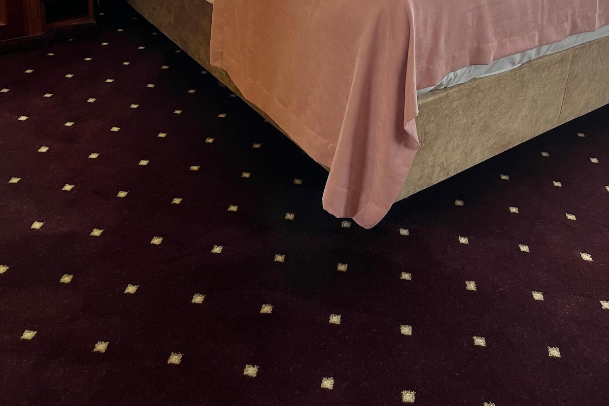 A hotel room with a large bed, wooden paneling, a small desk with a lamp, and a patterned carpet.