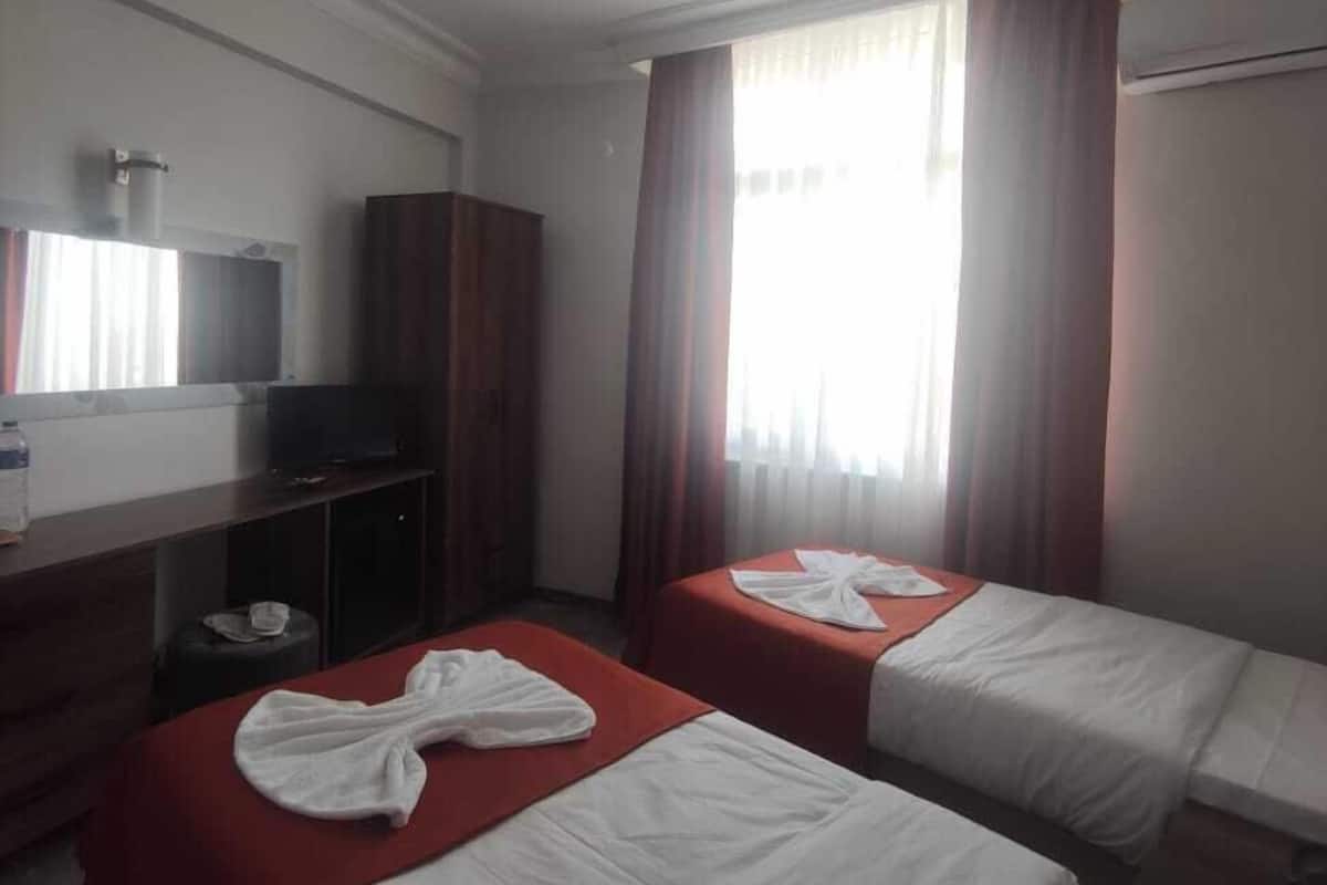 A hotel room with two beds, a TV, a wardrobe, and a window with curtains.