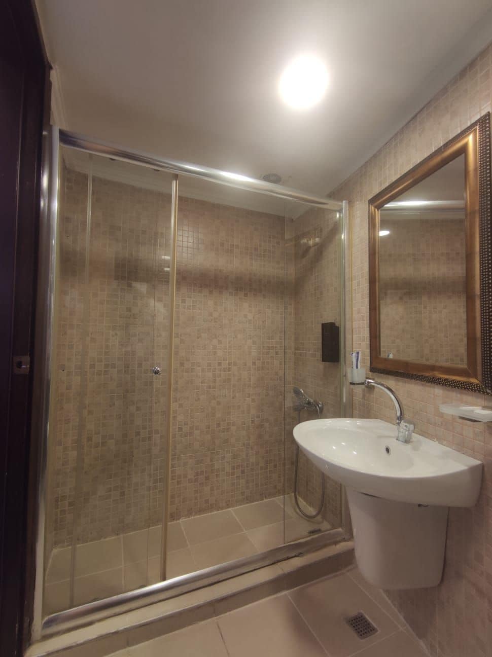 Un baño con ducha acristalada, lavabo blanco y espejo con marco de madera.
