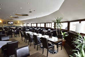 Un vaste espace dédié à la salle à manger, avec de nombreuses tables et chaises, de grandes fenêtres et des luminaires au plafond.