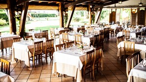 Un espacio de comedor al aire libre cubierto con mesas dispuestas para comensales, con sillas de madera y manteles blancos.