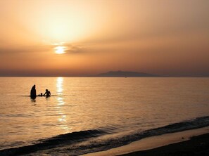 A sunset over a calm sea with a silhouette of a person and a child in the water. - Podere Giulio (Tarquinia)