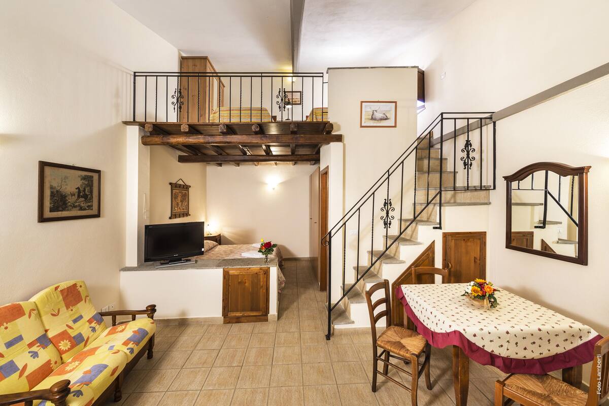 A cozy living room with a sofa, a TV, a dining table with chairs, and a staircase leading to an upper level.