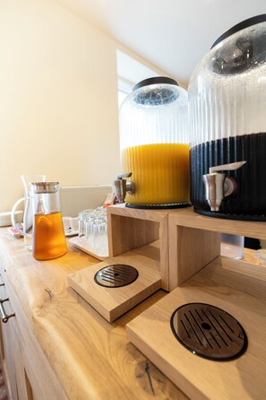 A wooden counter with a coffee maker, a glass carafe, and a large insulated mug filled with a yellow liquid.