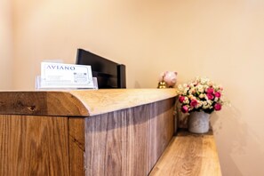 A wooden reception desk with a business card holder displaying "AVIANO" and a small piggy bank.