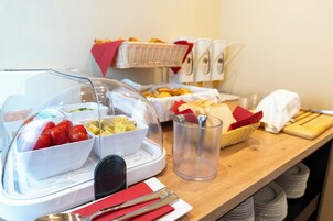 A buffet setup with a variety of food items, including a bowl of tomatoes, a basket of bread, and a clear glass pitcher.