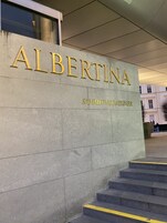 A building entrance with the name 'ALBERTINA' and 'SAMMLUNG BATLINER' in gold lettering on a grey stone facade.