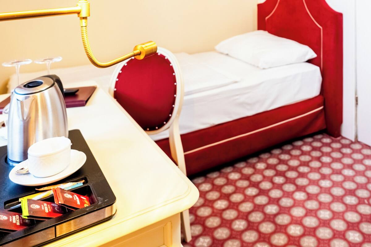 A hotel room with a bed, a bedside table with a lamp, a coffee maker, and a tray with tea bags.