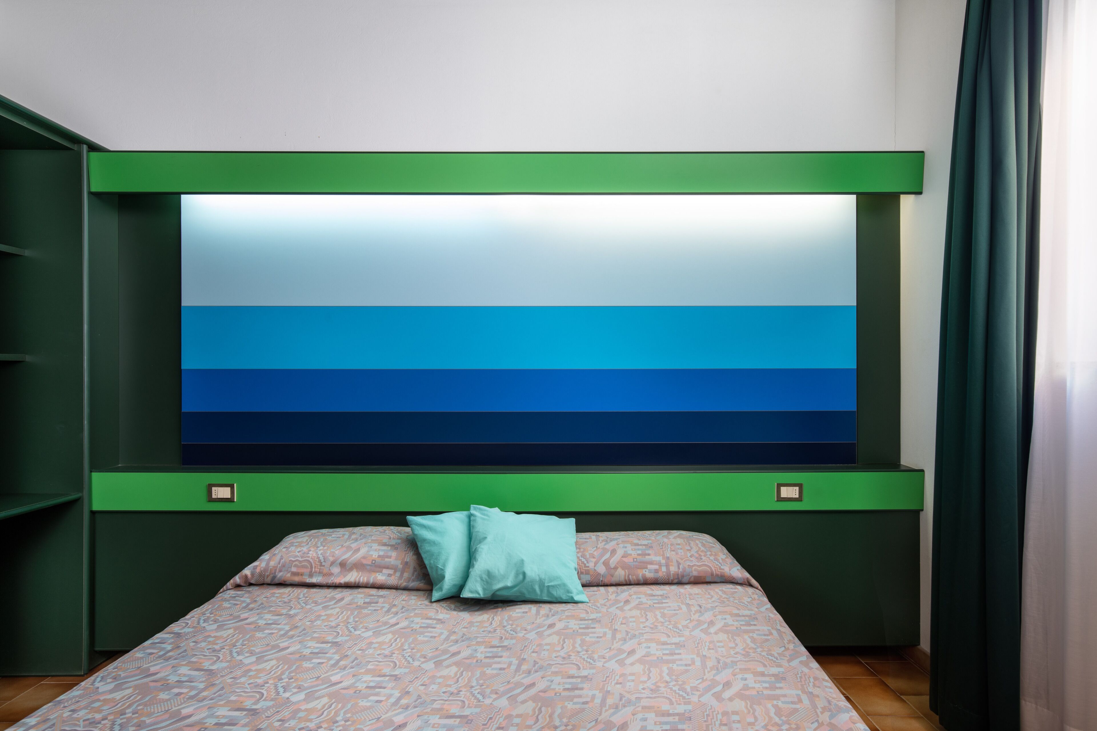 Une chambre à coucher avec un lit, un grand téléviseur fixé au mur et une tête de lit verte.