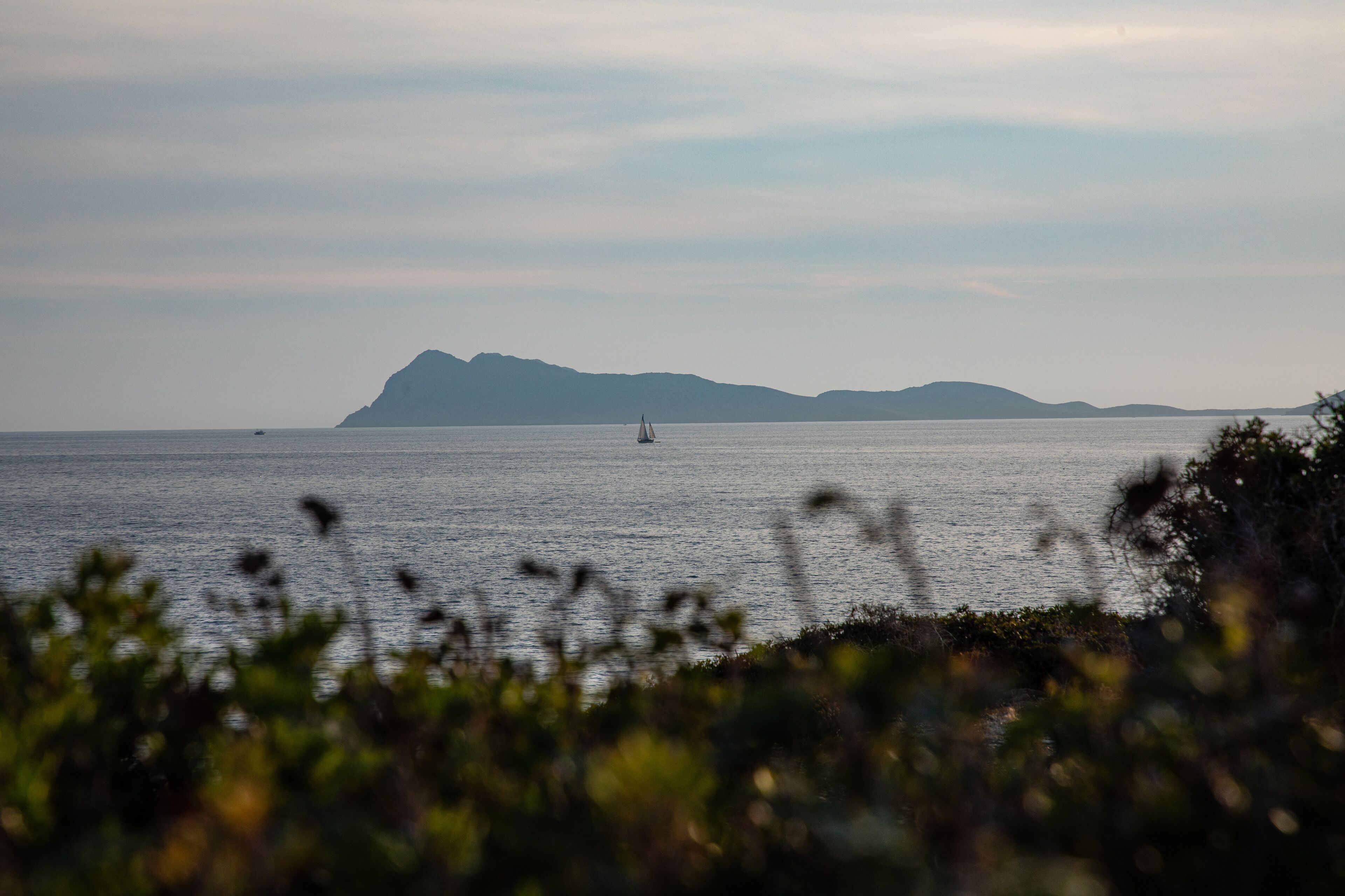 A calm sea with a sailboat and distant mountains.