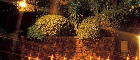 An outdoor dining area with tables and chairs, a pool, and a building with a stone wall and plants.