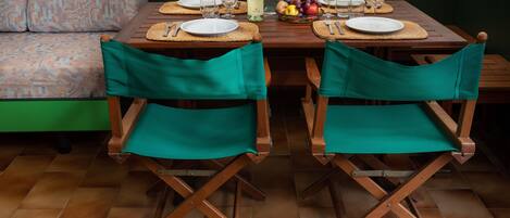 A dining area with a wooden table set for two, surrounded by green upholstered chairs.