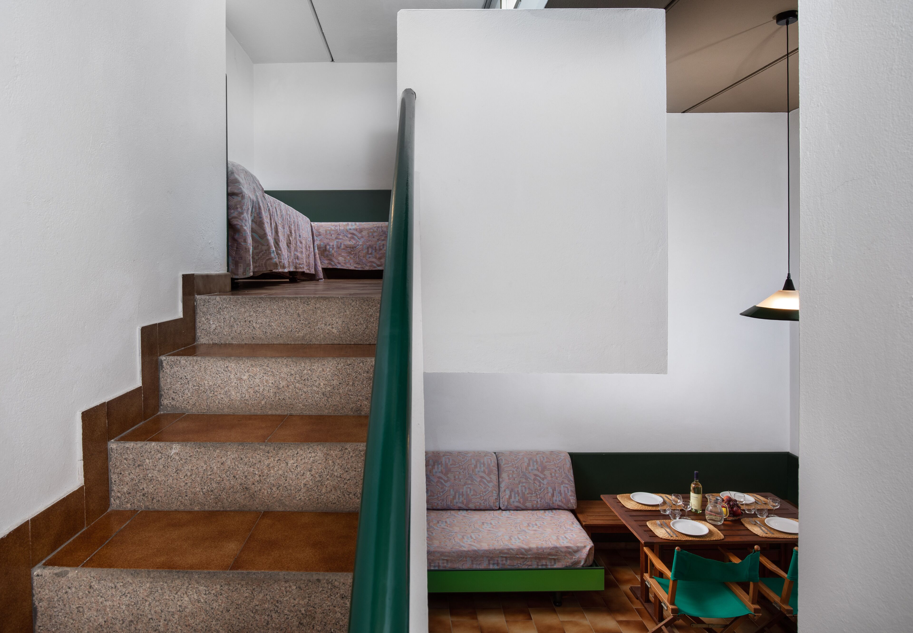 Un escalier avec une rampe verte mène à un espace détente où une table est dressée pour le repas.