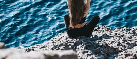 A person sitting on a rocky surface by the sea, with waves in the background.
