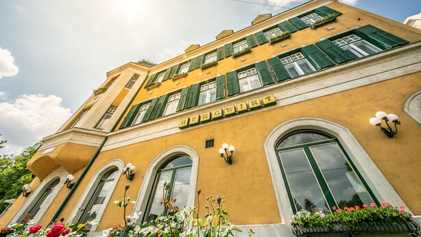Un edificio con fachada amarilla, contraventanas verdes y el nombre 'BERGWIRT' en la parte frontal.