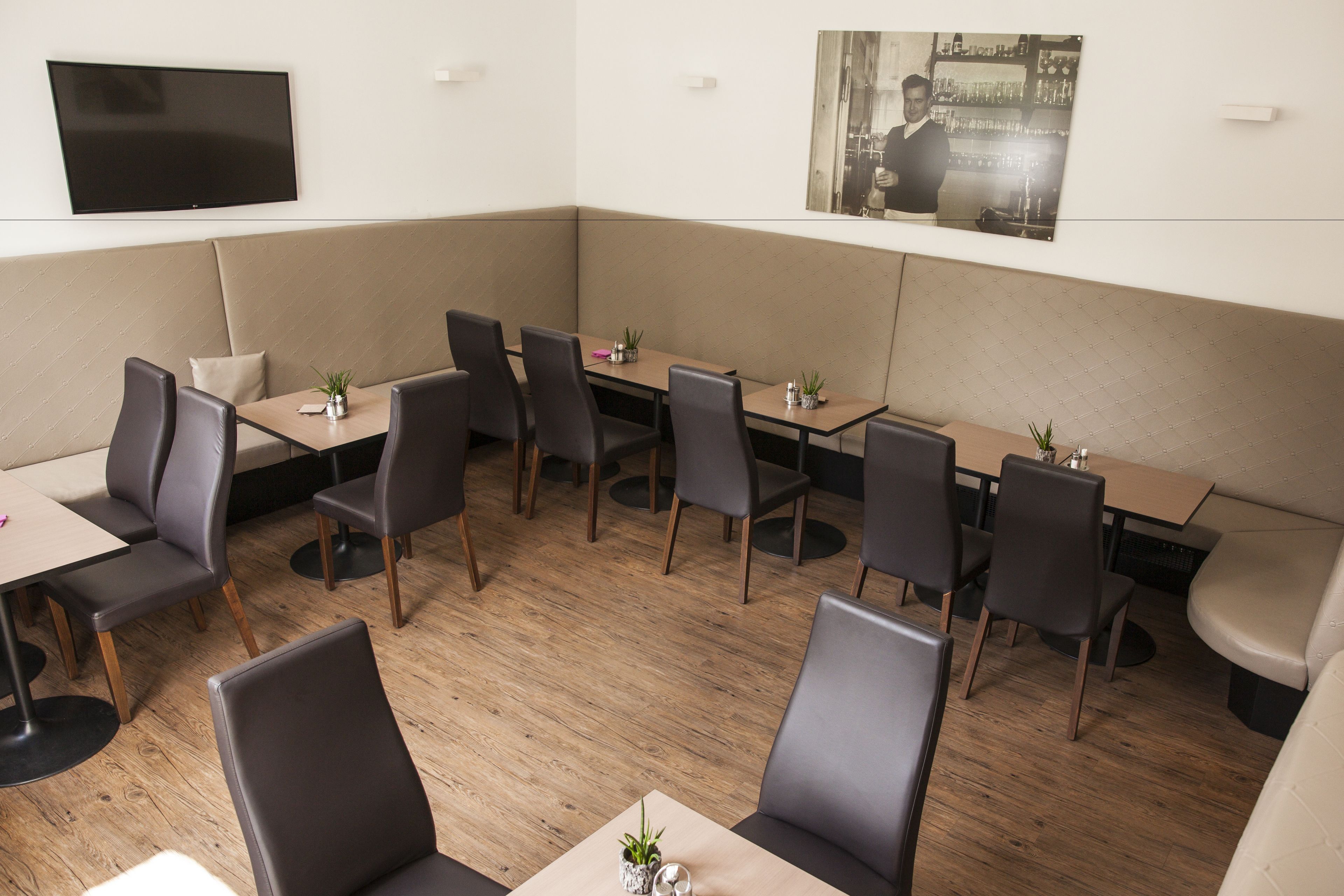Un restaurante moderno con cabinas y mesas, un televisor de pantalla plana en la pared y un cuadro enmarcado sobre la zona de estar.