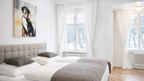 Un dormitorio con una cama grande, cabecera, dos ventanas con cortinas blancas y un cuadro de un perro en la pared.