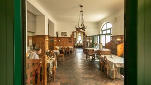 Un comedor con mesas y sillas de madera, una araña y vistas al exterior.