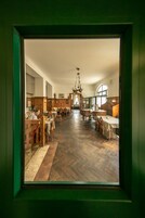 Zona pranzo con tavoli e sedie in legno, un lampadario e vista attraverso una finestra.