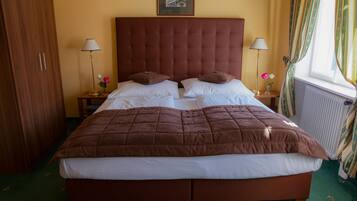 Un lit double avec une couette marron, deux tables de chevet avec des lampes, un tableau encadré au-dessus du lit et une fenêtre avec des rideaux.