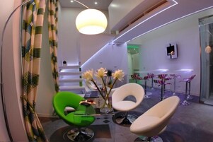 Un interno moderno con una sedia verde, sedie bianche, un vaso con fiori e una scala.