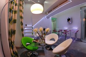 Un intérieur moderne avec un fauteuil vert, des chaises blanches, un vase de fleurs et un escalier.
