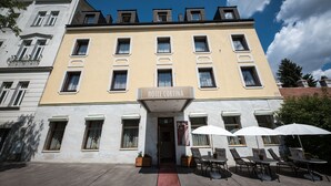 A hotel with a yellow facade, multiple windows, and outdoor seating with umbrellas. - Club Hotel Cortina (Vienna)
