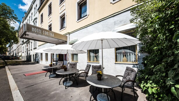 A hotel exterior with outdoor seating, including tables and chairs, and a sign reading "HOTEL CORTINA". - Club Hotel Cortina (Vienna)
