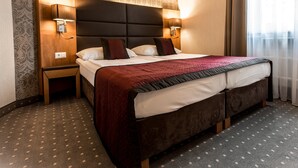 A hotel room with a large bed, two bedside tables, a headboard, and a patterned wallpaper. - Club Hotel Cortina (Vienna)