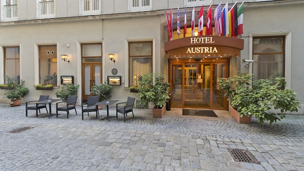 A hotel entrance with a cobblestone courtyard, outdoor seating, and multiple flags. - Hotel Austria (Vienna)