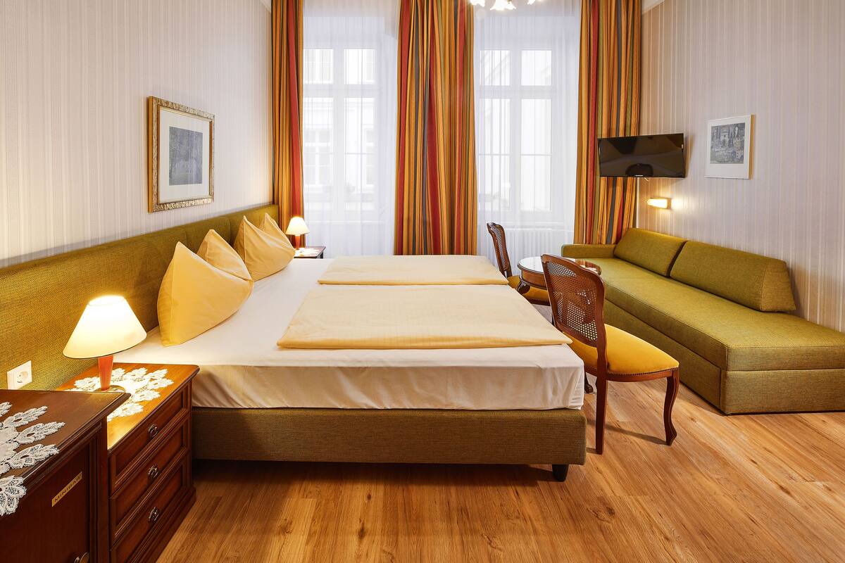 Une chambre d’hôtel avec un grand lit, un canapé, une table de chevet en bois et un téléviseur.