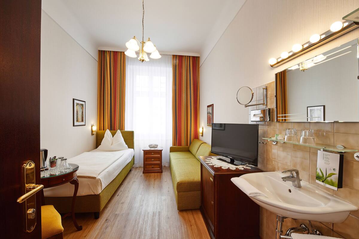 Une chambre d’hôtel comprenant un lit, un bureau, une télévision, une salle de bain avec un lavabo et un miroir, et une fenêtre avec des rideaux.